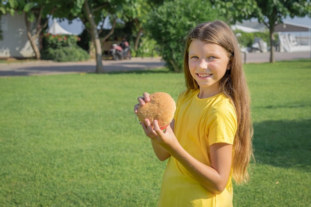 Adolescente feliz comendo um hambúrguer no parque ao ar livre