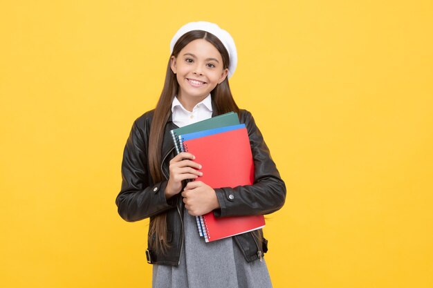 Adolescente feliz de volta à escola segurando livros de fundo amarelo, educação.