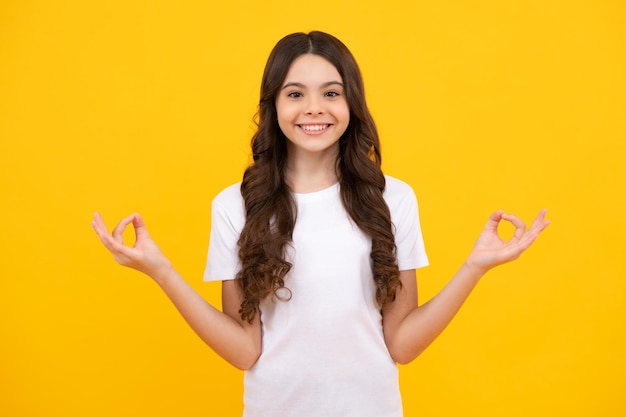 Adolescente feliz emociones positivas y sonrientes de niña adolescente Niño adolescente con camisa blanca tome las manos en yoga om aum gesto relajarse meditar intente calmar aislado sobre fondo amarillo