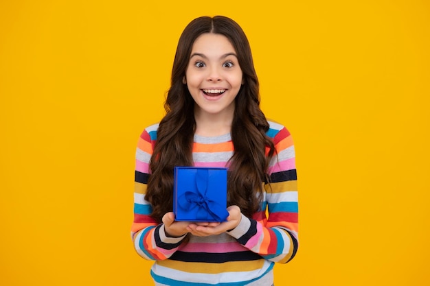 Adolescente feliz emociones positivas y sonrientes de niña niño Niño adolescente con caja presente sobre fondo amarillo aislado Niña adolescente dando regalo de cumpleaños Saludo actual y concepto de obsequio