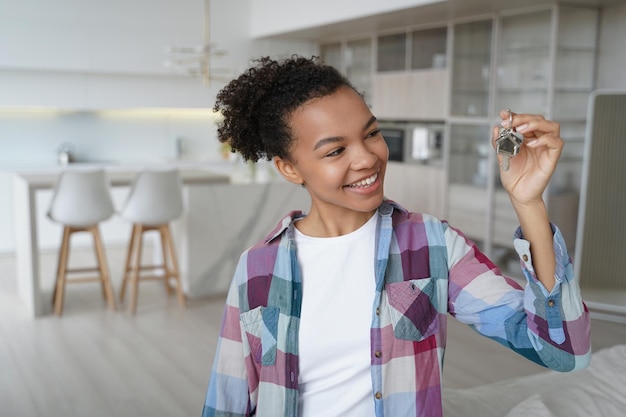 Adolescente feliz es dueña de casa en la sala de estar de la nueva residencia Chica sosteniendo la llave del nuevo apartamento