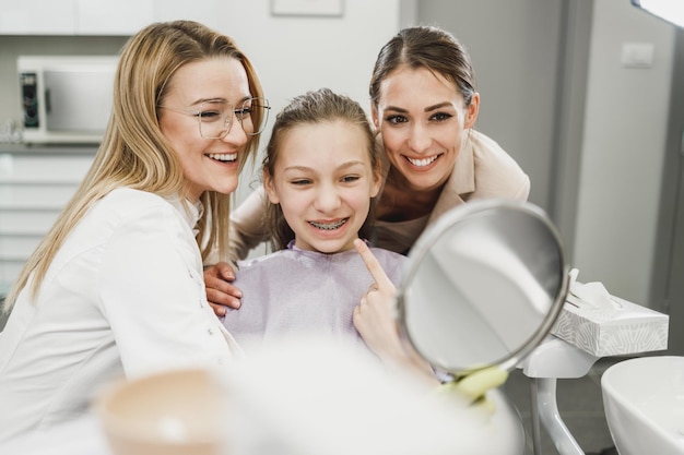 Una adolescente feliz mirando sus dientes en un espejo después de un procedimiento dental en el consultorio del dentista.