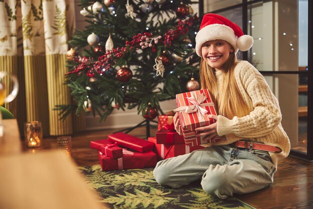 Adolescente feliz que se sienta en el árbol de navidad