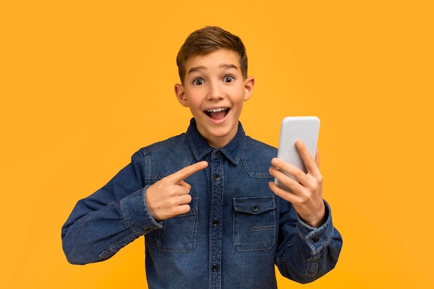 Un adolescente feliz señalando su teléfono inteligente con una expresión emocionada