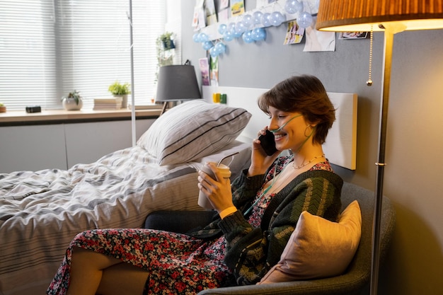 Adolescente feliz sentado en un sillón y hablando por teléfono móvil