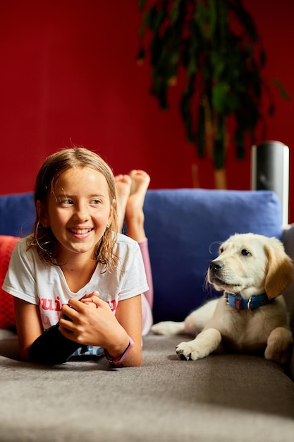 Una adolescente feliz tirada en el sofá y abrazando a su cachorro golden retriever