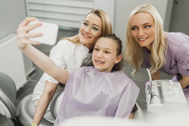 Una adolescente feliz tomando un sellfie con su dentista en el consultorio del dentista.