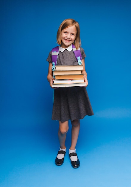 Una adolescente feliz con uniforme escolar sostiene una pila de libros Banner de una colegiala Retrato de una colegiala con espacio para copiar sobre un fondo azul