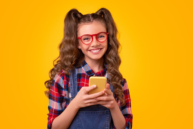 Adolescente femenina alegre en traje casual y gafas mirando mientras usa la aplicación móvil en el teléfono inteligente