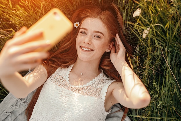 Adolescente femenina despreocupada tomando selfie mientras está acostado sobre el césped