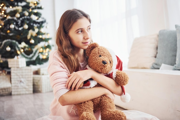 Adolescente feminino bonito dentro de casa na sala de estar na época dos feriados com ursinho de pelúcia.