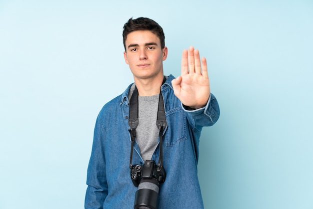 Adolescente fotógrafo hombre aislado sobre fondo azul haciendo detener el gesto con la mano