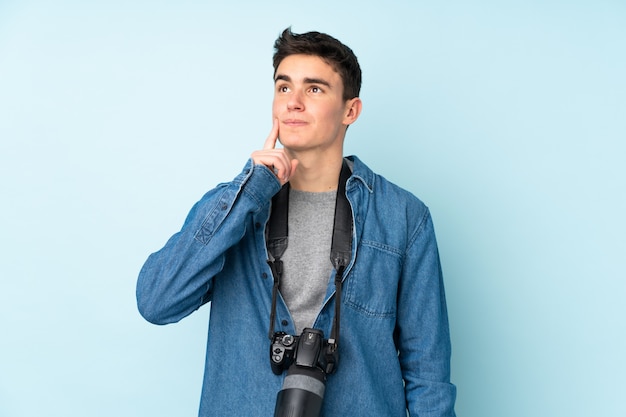 Adolescente fotógrafo hombre aislado sobre fondo azul pensando en una idea