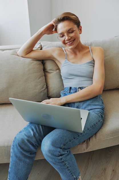 Adolescente freelancer com laptop sentada no sofá em casa sorrindo em roupas de casa e óculos com corte de cabelo curto estilo de vida sem filtros espaço de cópia livre foto de alta qualidade