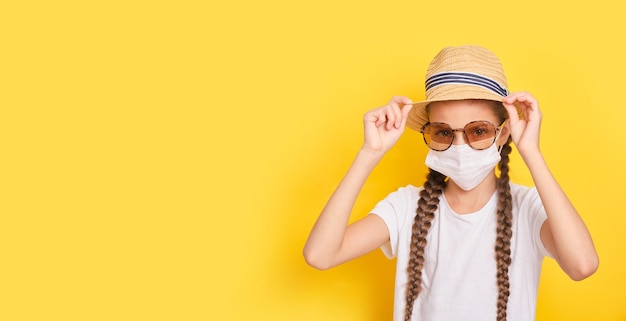 Adolescente en gafas de sol de mascarilla médica y sombrero de paja sobre fondo amarillo concepto de vacaciones