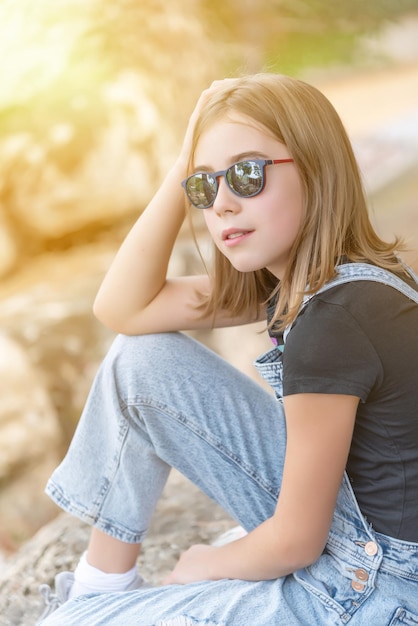 Adolescente con gafas de sol y ropa informal sentada mirando al horizonte