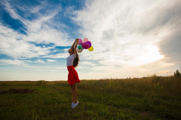 Una adolescente con globos se para en el campo y siente el viento