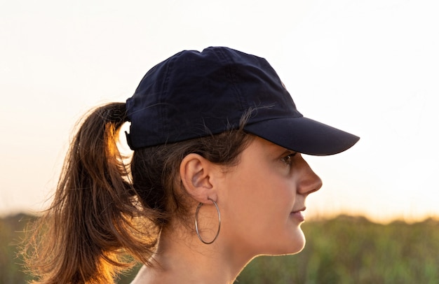 Adolescente con gorra de béisbol azul oscuro al atardecer. Chica adolescente de media cara. Maqueta de gorra