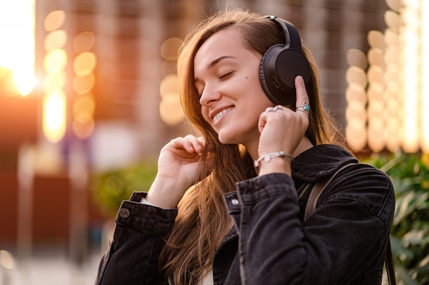 Adolescente gosta e ouve música em fones de ouvido sem fio pretos enquanto caminha pela cidade