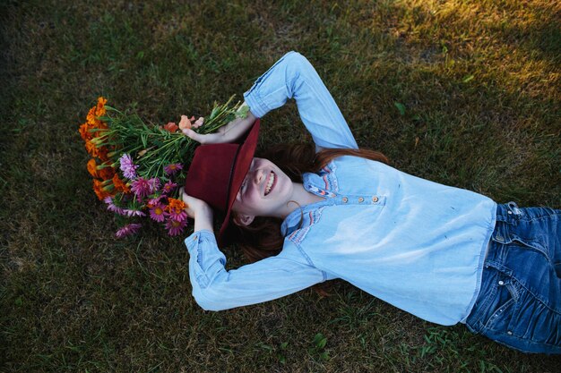 Adolescente con un gran sombrero rojo está tumbado en el césped con un ramo de flores multicolores