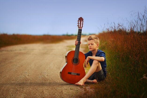 Adolescente con guitarra acústica en carretera.