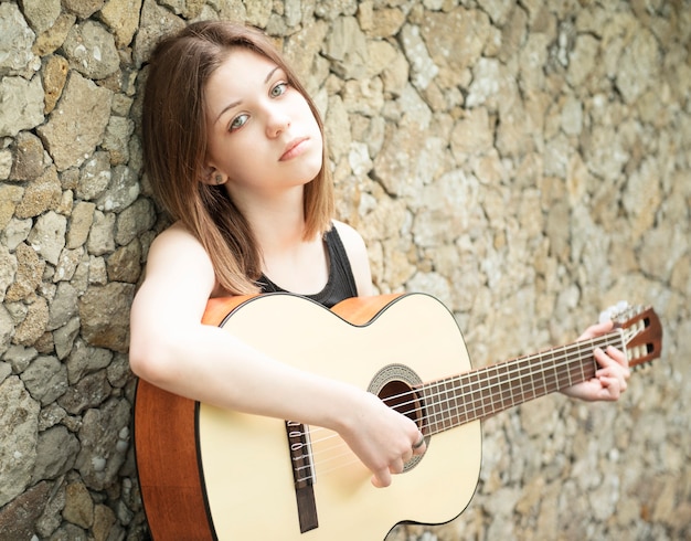 Foto adolescente con una guitarra contra una pared marrón