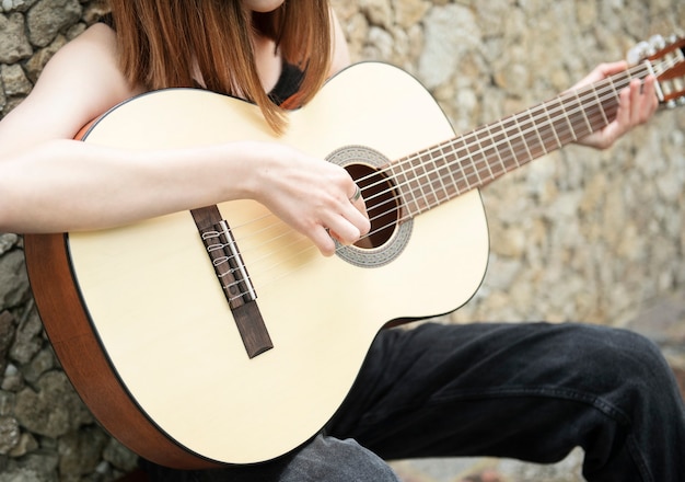 Adolescente con una guitarra contra una pared marrón