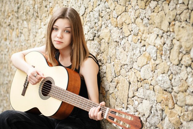 Adolescente con una guitarra contra una pared marrón