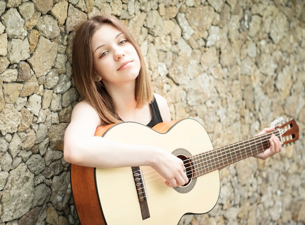 Adolescente con una guitarra contra una pared marrón