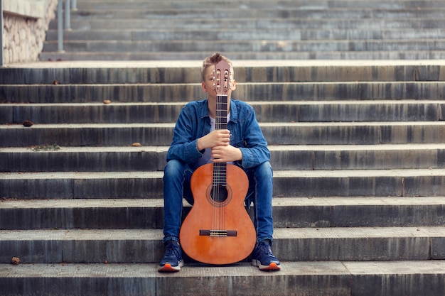 Adolescente con guitarra sentado en los escalones del parque