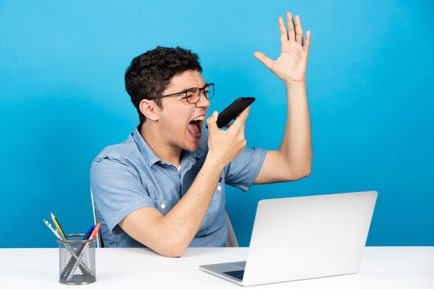 Adolescente hispânico irritado gritando no telefone isolado em fundo azul