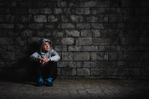 Adolescente hispano deprimido sentado contra una pared en la oscuridad. Ansiedad y depresión en el concepto de adolescencia.