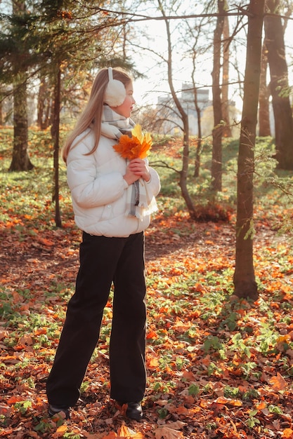 Adolescente con hojas de otoño mirando hacia otro lado usando ropa informal en un parque de otoño al aire libre