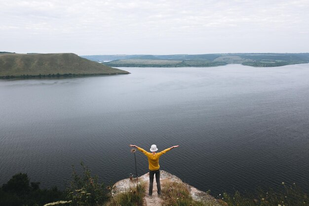 Adolescente inconformista en jersey amarillo de pie en la cima de la montaña de roca y levantando las manos Chico elegante joven explorando y viajando Momento atmosférico Copiar espacio