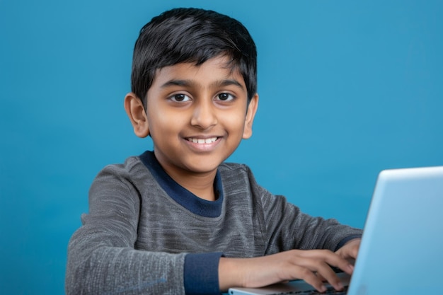 Un adolescente indio sonriente usando una computadora portátil para estudiar en línea sobre un fondo azul.