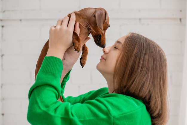 Adolescente en jeans y suéter verde sostiene un pequeño perro salchicha en sus brazos. mascota favorita. la chica abraza, besa, aprieta a su amado perro en sus manos. cuidado animal. espacio para texto. foto de alta calidad