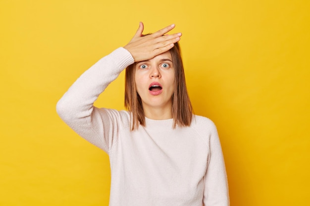 Una adolescente con un jersey con colas de caballo aislada sobre un fondo amarillo hace que la palma de la cara se sienta sorprendida y asustada estando sola mirando la cámara con los ojos grandes y la boca abierta