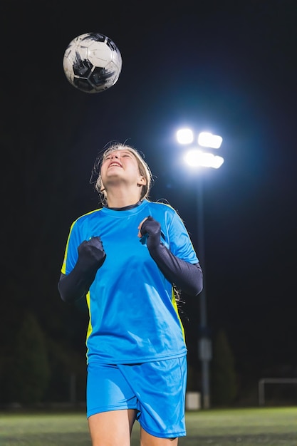 Adolescente jogadora de futebol com roupas esportivas jogando uma bola de futeball no ar no treino de futebal