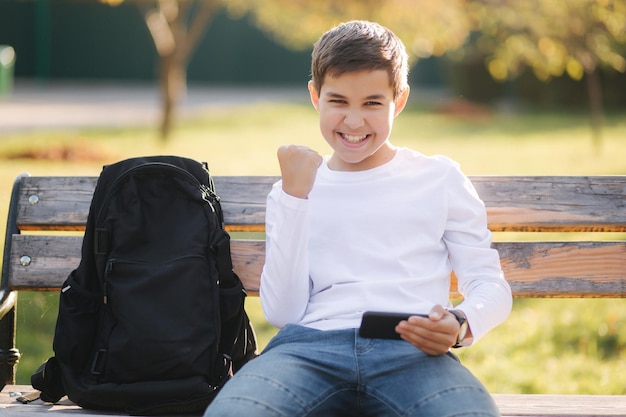 Adolescente juega juegos en línea en su teléfono inteligente en el parque después de clases en la escuela