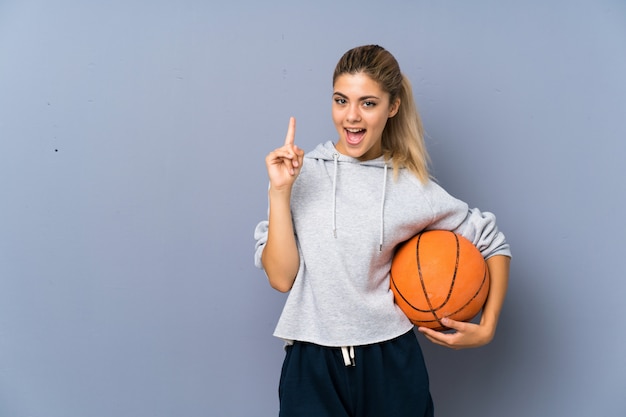 Adolescente jugando baloncesto sobre la pared gris con la intención de darse cuenta de la solución mientras levanta un dedo