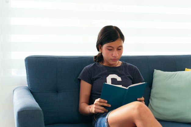 Adolescente latina se sienta leyendo un libro en casa