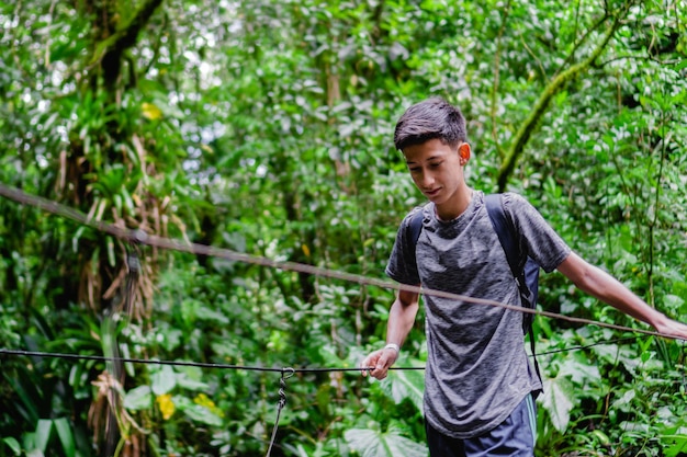 Adolescente latino en la selva cruzando un puente colgante caminata ecológica en colombia