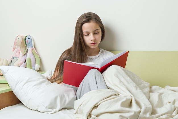 Adolescente lee un cuaderno escolar en la cama.