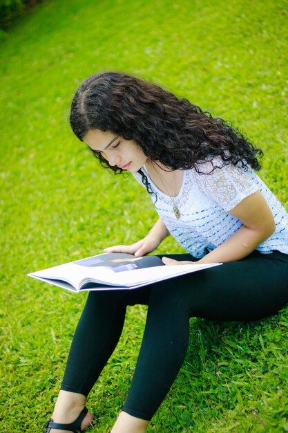 Foto una adolescente leyendo un libro en el parque.