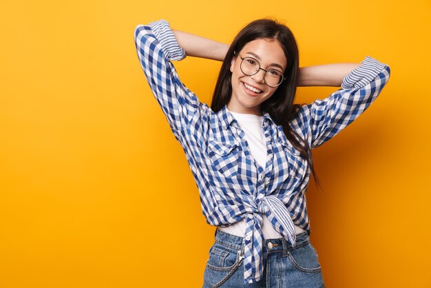 una adolescente linda joven feliz optimista positiva en vidrios que presenta aislada sobre la pared amarilla.