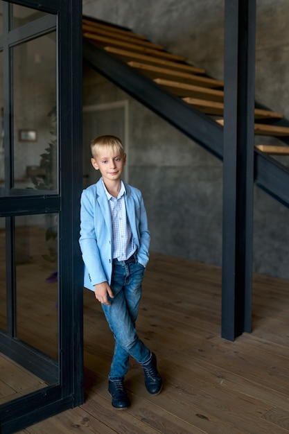 Foto adolescente loira, com uma camisa elegante e calça jeans, fica em um apartamento estilo loft e sorri amplamente