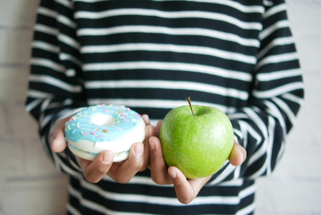 Adolescente mano sosteniendo donuts y manzana