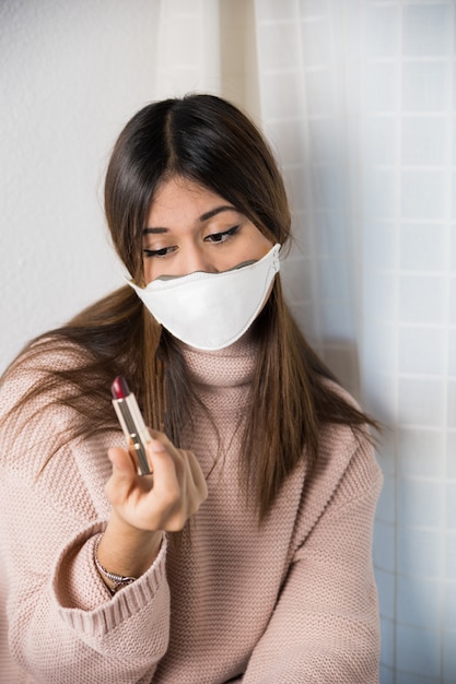 Foto una adolescente con una máscara protectora en la cara y un lápiz labial en la mano.