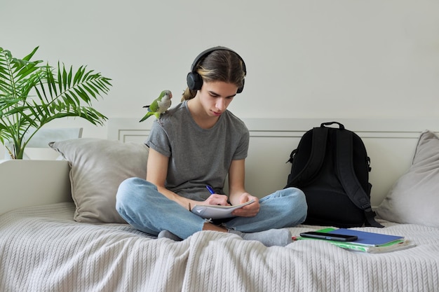 Adolescente masculino com estudante de papagaio de estimação sentado em fones de ouvido em casa