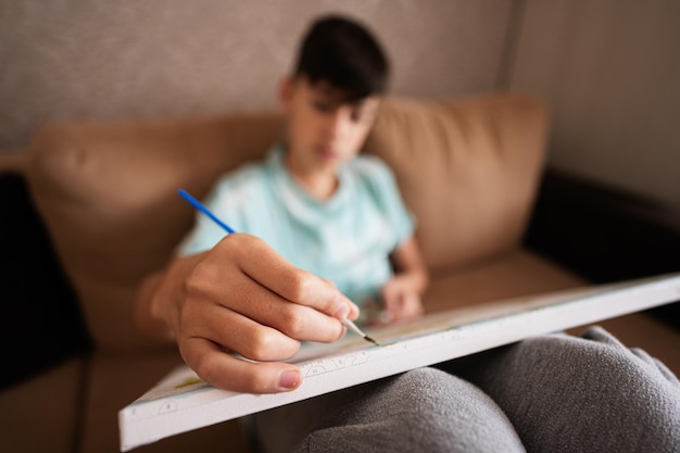 Adolescente masculino joven pintando un cuadro por números sobre lienzo en la sala de estar en casa Hobby y ocio c